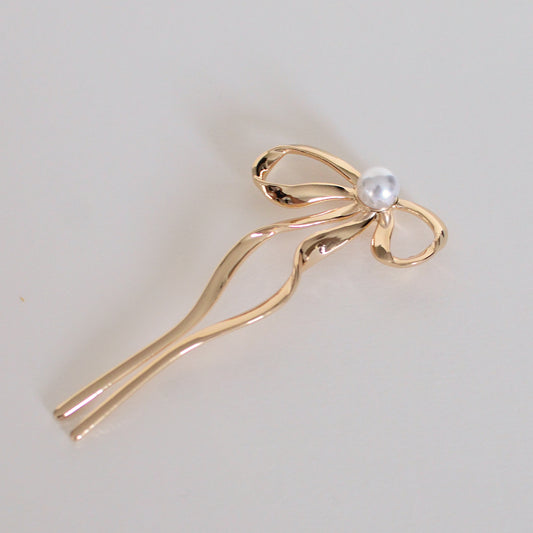 Gold hair clip with a pearl on a light gray background