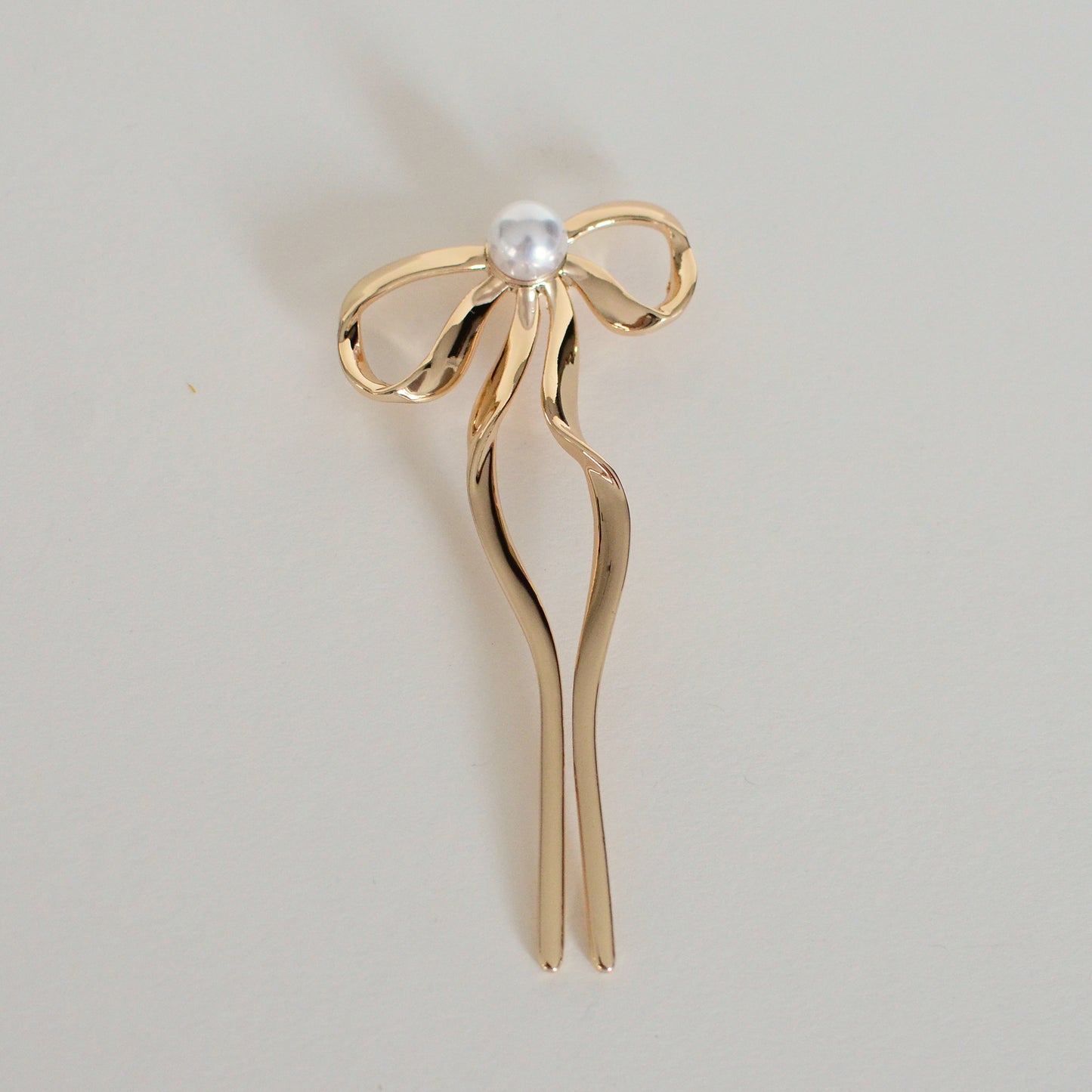 Gold hair stick with a pearl on a light gray background